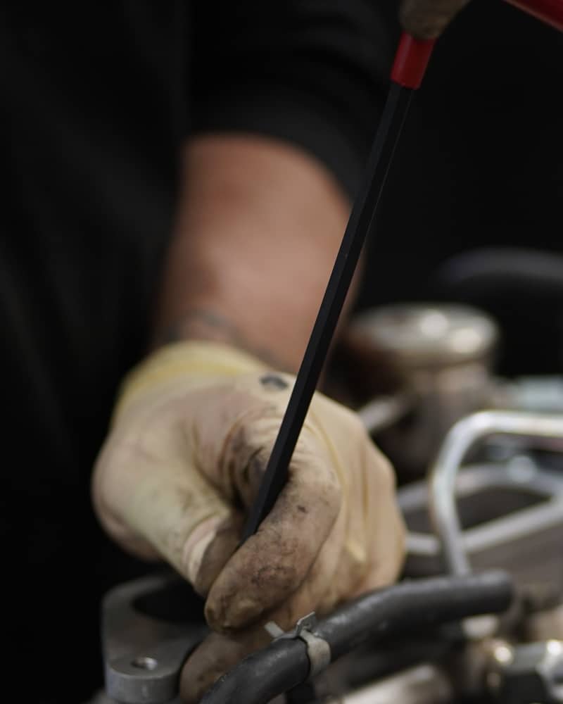 A gloved hand turning a T-handle wrench over an engine