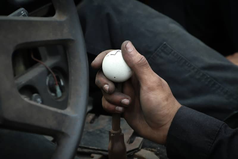 A mechanic's hand resting on a worn shift knob inside a truck cab