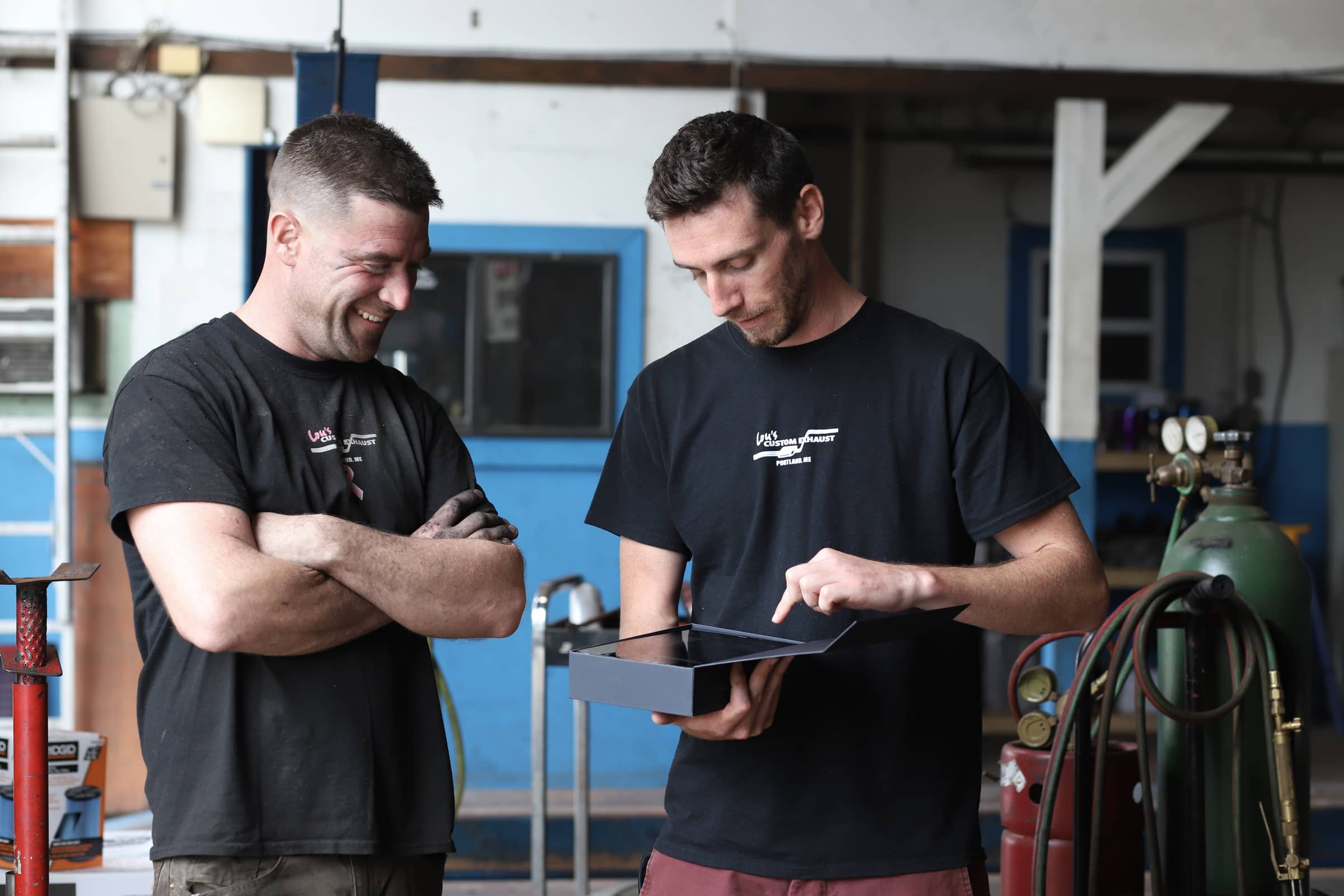 Two tradesmen in a shop reviewing work together on a tablet