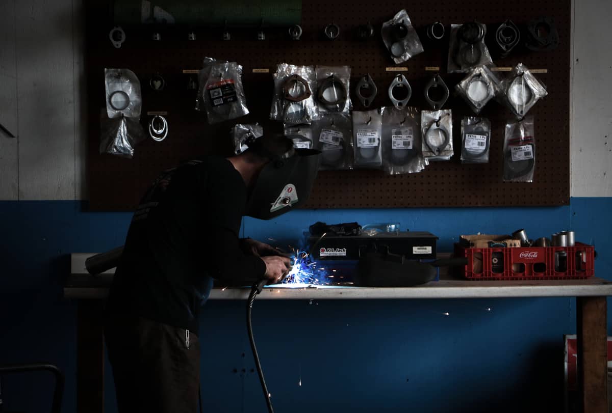 A welder working at a bench beneath a wall of packaged gaskets